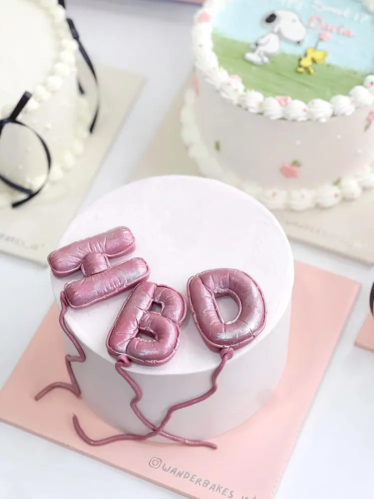 Cake putih dengan balon HBD berwarna pink metalik