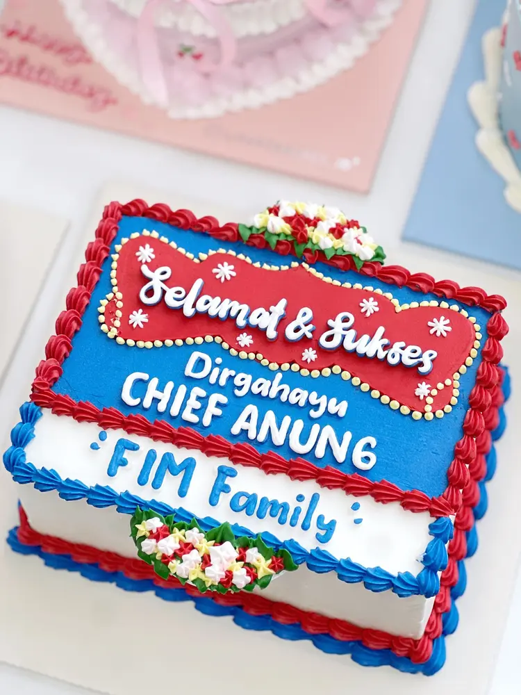 Cake persegi bergaya papan bunga merah, biru dan putih bertuliskan Selamat & Sukses