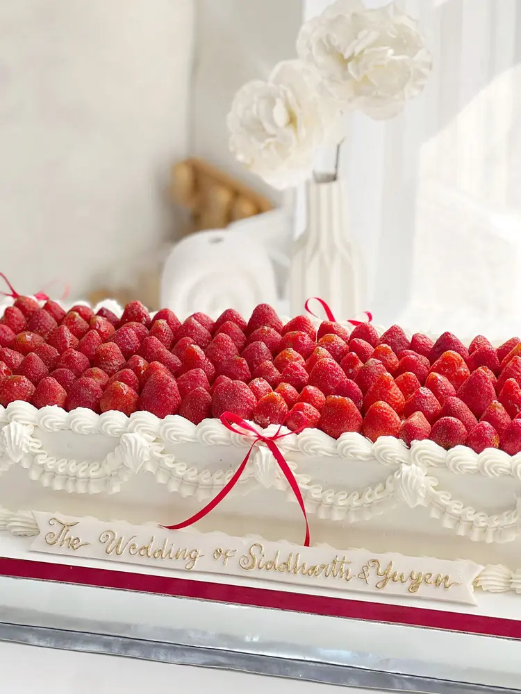 Long cake putih dengan barisan strawberry segar dan tulisan pernikahan