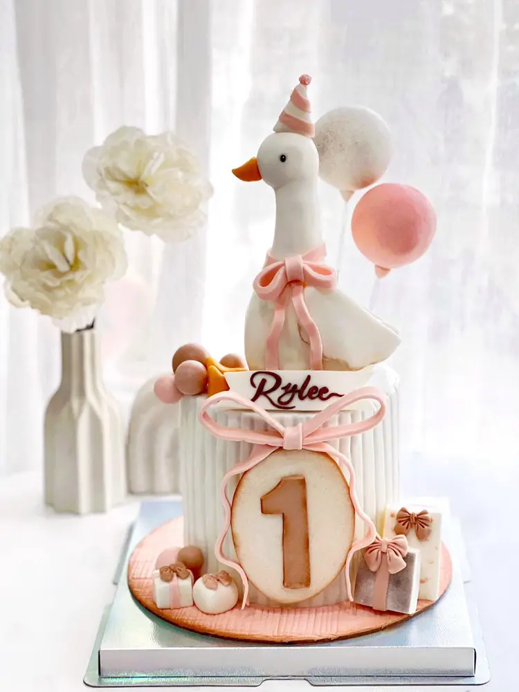 Cake putih bergaris dengan figur angsa, balon dan angka 1